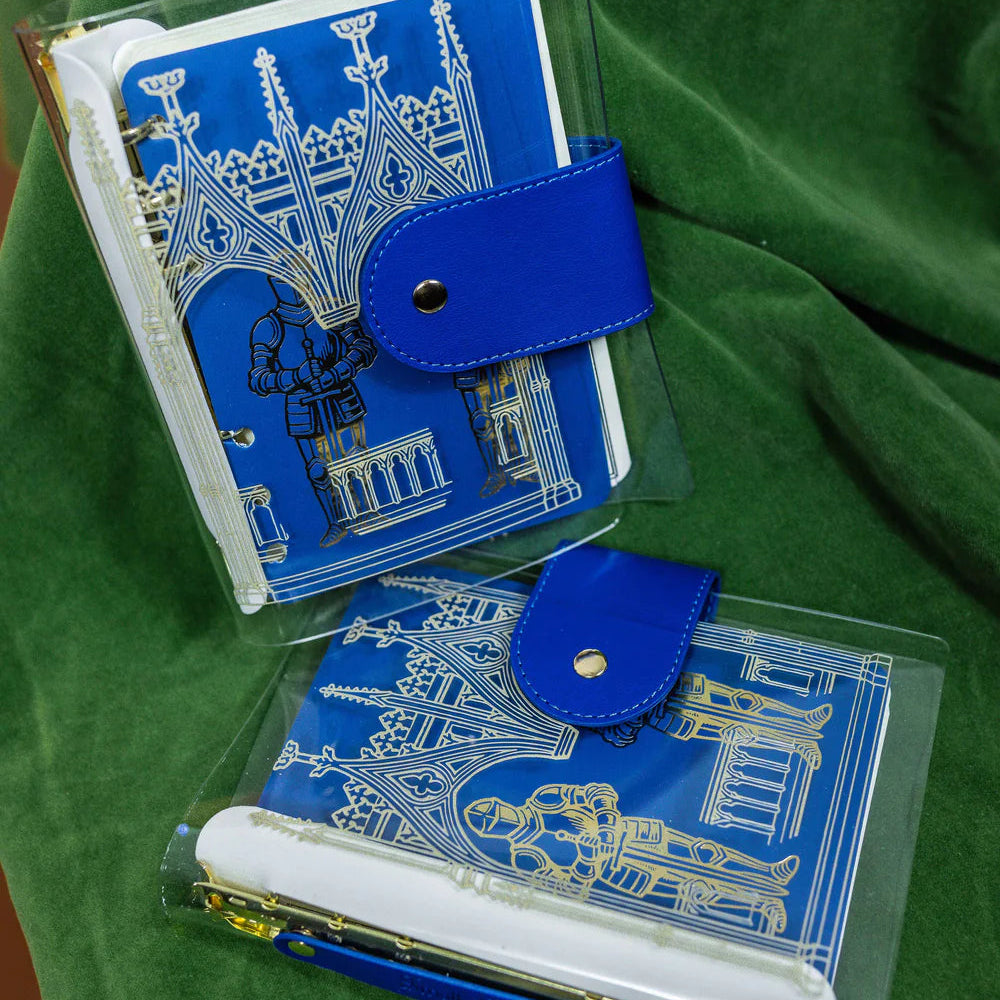 Step into a world of medieval wonder with this charming A6 binder notebook. Adorned with gothic architecture and noble knights rendered in shimmering golden foil, the cover transports you straight to a castle's grand halls.

Inside, a delightful coloring front page invites your creative touch, while 50 pages of luxurious cream 100 gsm paper await your thoughts, sketches, and stories. Perfect for journaling, note-taking, or artistic pursuits with a touch of enchantment.