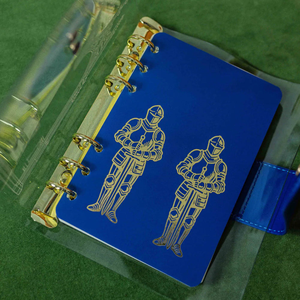 Step into a world of medieval wonder with this charming A6 binder notebook. Adorned with gothic architecture and noble knights rendered in shimmering golden foil, the cover transports you straight to a castle's grand halls.

Inside, a delightful coloring front page invites your creative touch, while 50 pages of luxurious cream 100 gsm paper await your thoughts, sketches, and stories. Perfect for journaling, note-taking, or artistic pursuits with a touch of enchantment.