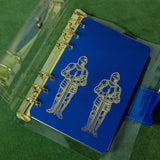 Step into a world of medieval wonder with this charming A6 binder notebook. Adorned with gothic architecture and noble knights rendered in shimmering golden foil, the cover transports you straight to a castle's grand halls.

Inside, a delightful coloring front page invites your creative touch, while 50 pages of luxurious cream 100 gsm paper await your thoughts, sketches, and stories. Perfect for journaling, note-taking, or artistic pursuits with a touch of enchantment.