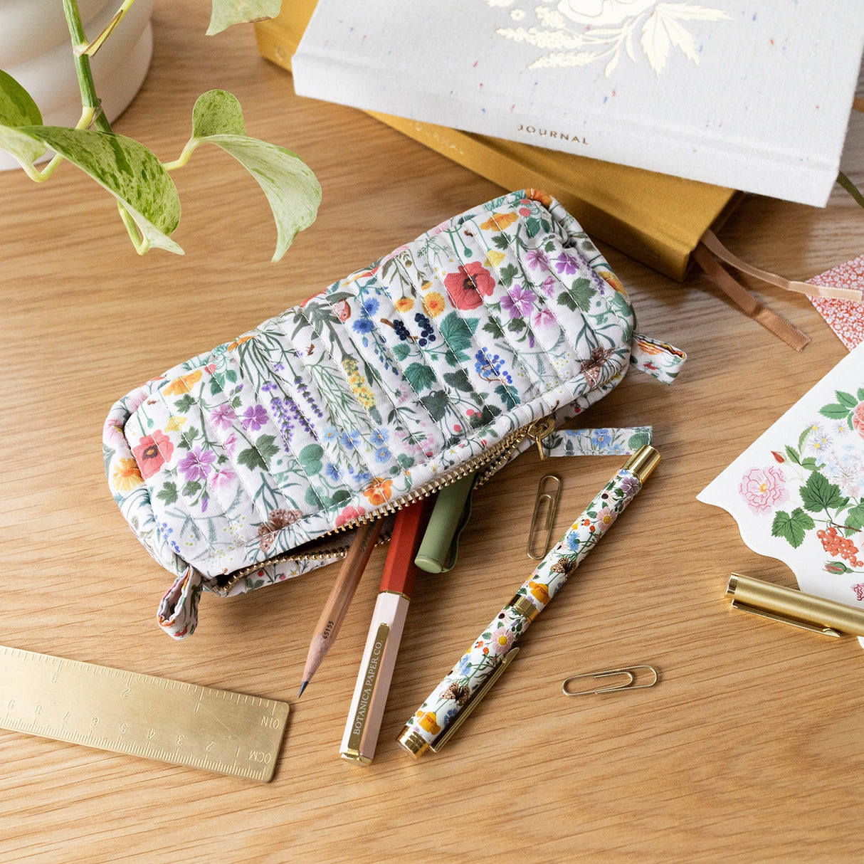 Each versatile pouch showcases premium quilted cotton in four distinct illustrated patterns, complemented by an elegant gold brass zipper with coordinating pull—adding a sophisticated finishing touch to these signature pieces.

Features:

Size: 7" x 3" x 2"
Premium quilted cotton exterior
Coordinating interior cotton lining
Gold brass zipper with matching pull
Versatile use as pencil pouch or makeup bag
Perfect for desk display or on-the-go organization