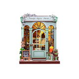 This elegant miniature captures the beauty of a boutique flower shop, adorned with delicate blooms, pastel accents, and a graceful arched doorway that invites you inside.

From the dainty floral arrangements to the hand-painted shop signs and warm, glowing interior, every detail evokes the feeling of strolling down the Champs-Élysées on a sunny afternoon. The soft LED lights cast a welcoming glow, highlighting rows of flowers ready to be wrapped for someone special.