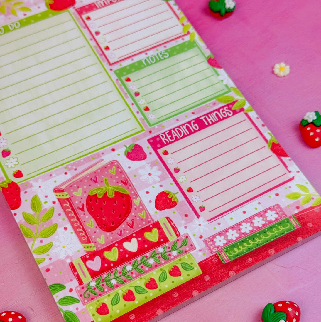 Stay organized in style with this adorable Strawberry Book Stack Daily Planner Notepad! Perfect for jotting down your daily tasks, goals, and bookish ideas, this notepads brings a pop of personality to your desk. Featuring a sturdy cardboard back and premium 70lb. uncoated paper, it's built to last through all your planning adventures.&nbsp;

✦ DETAILS ✦

Size: 5.5" x 8.5"

70 lb. Paper Uncoated

Padded With Cardboard Back

50 Sheets
No magnet backing