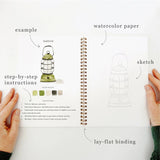 Twelve camping illustrations — a vintage camper, lantern, campfire, tent, canoe, s'mores, and more — each pre-outlined with step-by-step instructions. Paintings take about thirty minutes from start to finish, making it approachable for first-time painters and a favorite for gifting.