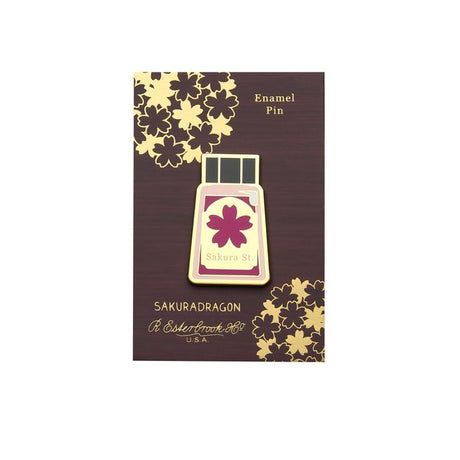 The Sakura Street Ink Lapel Pin turns one of the collection's coordinating ink bottles into a collectible hard enamel design. Measuring 4.5 cm and finished with gold-plated details, the pin carries the colors and imagination of Cindy Duong's Sakura Street artwork onto a jacket, bag, or display board.