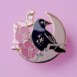 This enamel pin features a Jackdaw perching on a branch of pink orchid flowers, in front of a large gold moon. The pin is presented on a Glitter Punk backing card and is secured with 2 pin backs.

This pin is part of the Corvid Collection, an 8-part series of bird pins. 

Measurements: 35mm