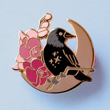 This enamel pin features a Jackdaw perching on a branch of pink orchid flowers, in front of a large gold moon. The pin is presented on a Glitter Punk backing card and is secured with 2 pin backs.

This pin is part of the Corvid Collection, an 8-part series of bird pins. 

Measurements: 35mm