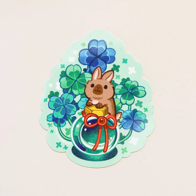 Sticker with a cartoon rabbit holding a clover and a bow on a light green background