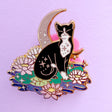 This super sweet fantasy pin features a black and white tuxedo cat relaxing on a lily pad in front of a crescent moon.

It’s 45mm (1.77”) wide, and is made from gunmetal hard enamel, with glitter and UV printed details. It's secured with 2 pink clutches to keep the pin in place.