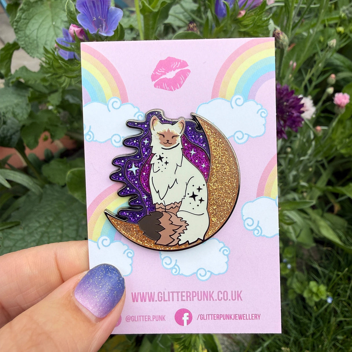 Calling all owners of a long haired pointed / meezer cats! This super cute design features the cat sitting in front of a sparkly moon with a glittery, starry sky in the background.

The pin is 40mm (1.57”) tall, and is made from gunmetal hard enamel, with glitter and UV printed details. It's secured with 2 pink clutches to keep the pin in place.