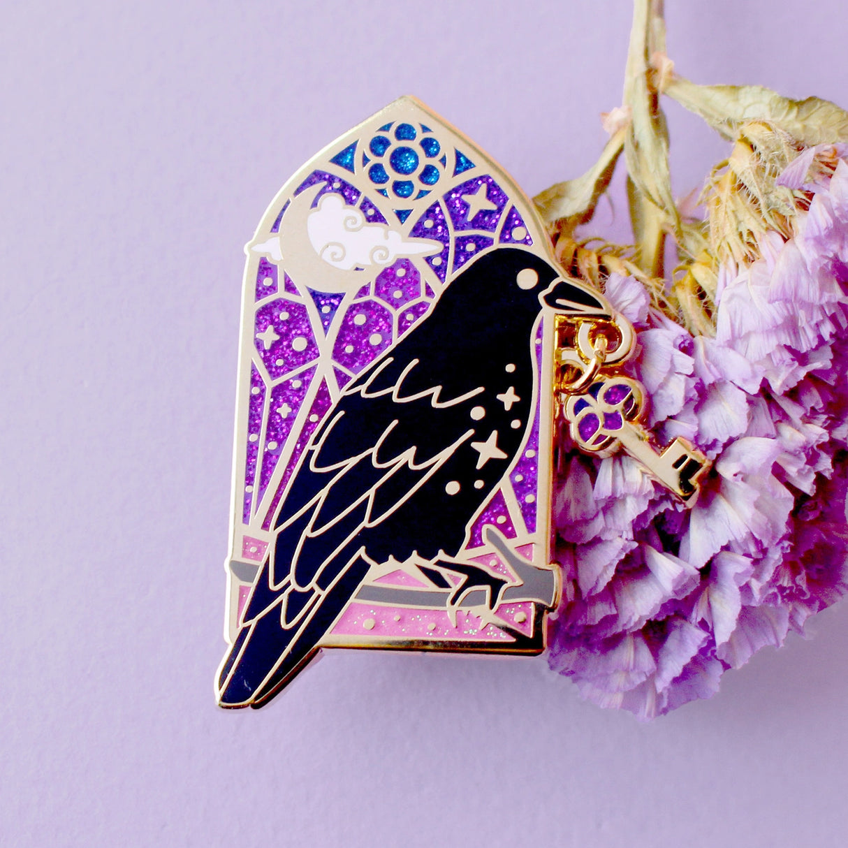 This enamel pin features a black crow holding a key in its beak, in front of a glittery blue and purple arched window. The pin is presented on a Glitter Punk backing card and is secured with 2 pin backs.

This pin is part of the Corvid Collection, an 8-part series of bird pins. 

Measurements: 45mm