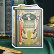 A humorous book-style greeting card that’s sure to spark a smile. This dark green and yellow vintage design features hand-illustrated chickens framed in ornate gold detailing with the playful phrase “Just chickin’ in on you.” A witty and collectible foil-pressed stationery piece that adds a touch of humor to your display.

Product Details:
- Dimensions: 5" x 7"
- Die-cut vintage book cover
- Hand-illustrated with gold foil details
- Blank interior
- Offset and foil printed
- Envelope included