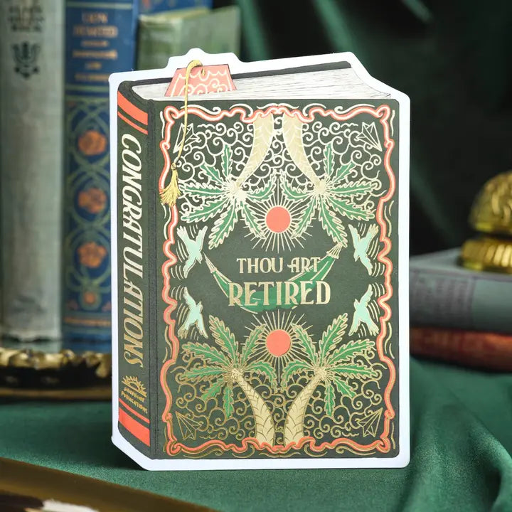 A witty book-shaped retirement card for those ready to begin their next chapter. This dark green vintage-style cover features golden palm trees and hammocks in a repeating pattern, with “Thou Art Retired” gleaming across the front in gold foil. A perfect mix of humor and elegance for celebrating well-earned rest.

Product Details:
- Dimensions: 5" x 7"
- Die-cut vintage book design
- Hand-illustrated with gold foil accents
- Blank inside
- Offset and foil printed
- Envelope included
