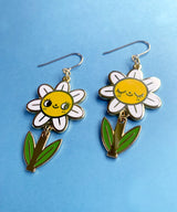 A pair of mis-matched happy daisy themed earrings (one one with happy open eyes, and one with happy closed) with separate dangling stems. Made from hard enamel with shiny gold metal finish on high quality Hypo-Allergenic, gold plated, brass based hooks.

Each earring measures approximately 5cm tall x 3cm wide. Earrings come in a Hannakin embossed gift box.