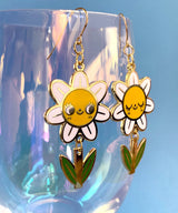 A pair of mis-matched happy daisy themed earrings (one one with happy open eyes, and one with happy closed) with separate dangling stems. Made from hard enamel with shiny gold metal finish on high quality Hypo-Allergenic, gold plated, brass based hooks.

Each earring measures approximately 5cm tall x 3cm wide. Earrings come in a Hannakin embossed gift box.