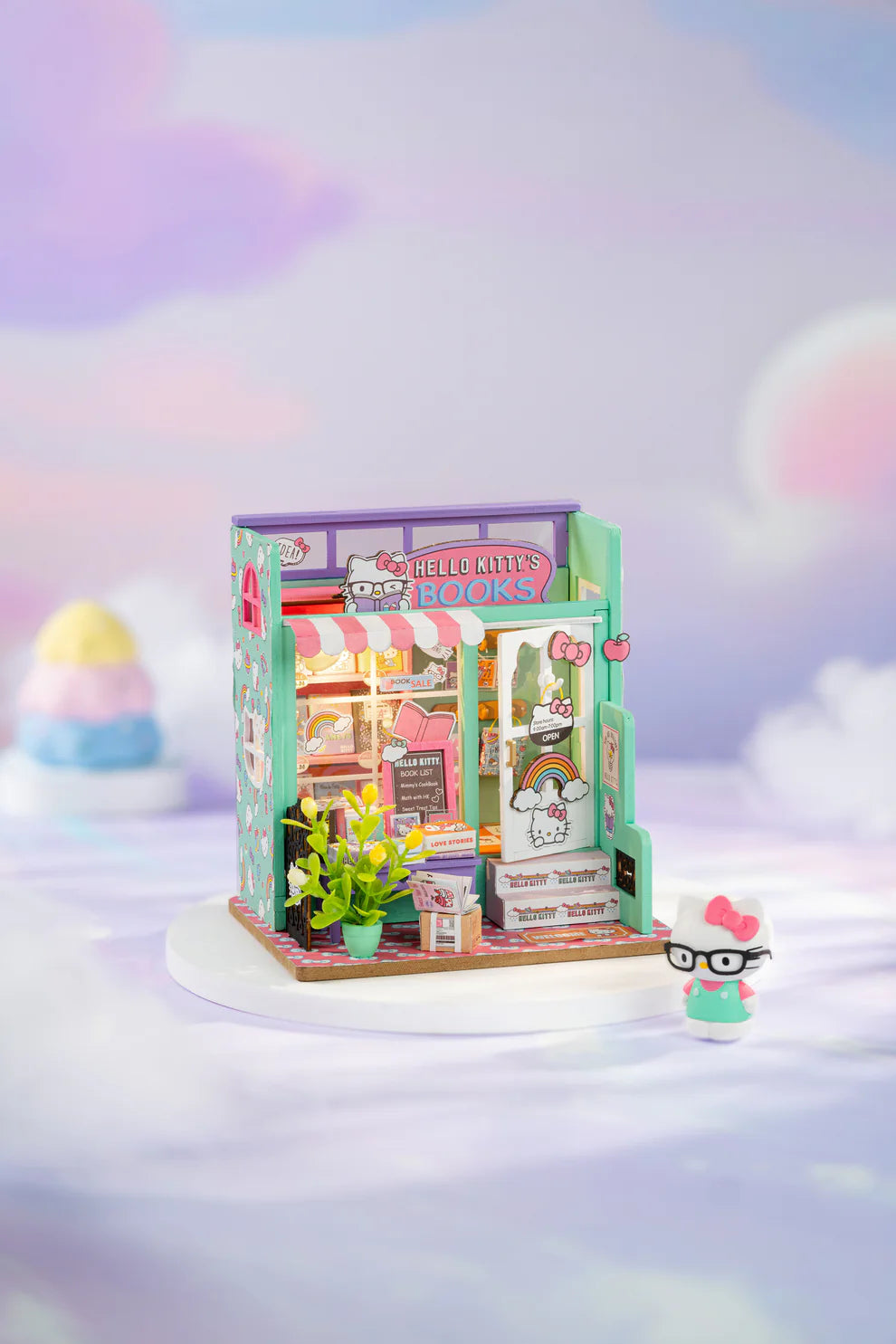 Step into the charming world of Hello Kitty with this delightful miniature house kit, where she runs her very own bookstore. Filled with tiny books, adorable gifts, and colorful gift bags, this kit is decorated in Hello Kitty's iconic style. The charming "open" sign welcomes you into the cozy shop, where a little lamp lights up the interior, creating a warm and inviting atmosphere. Perfect for fans and crafters alike, this kit offers hours of fun and a beautiful keepsake to treasure.