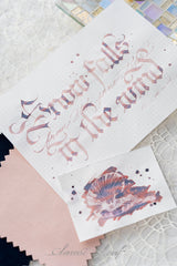 Snow Falls From the Pine Tips in the Wind is a serene winter ink that captures the quiet beauty of snowfall drifting through a forest at dawn. This multi‑shading fountain pen ink blends a soft rose‑mauve base with cool lavender and deep indigo shadows, creating a gentle, atmospheric palette that shifts with nib pressure and paper texture.