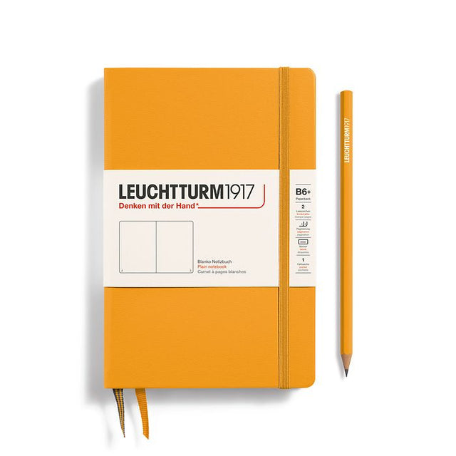 A hardcover Leuchtturm1917 Rising Sun notebook in orange color with a matching orange pencil, both featuring the brand's logo.