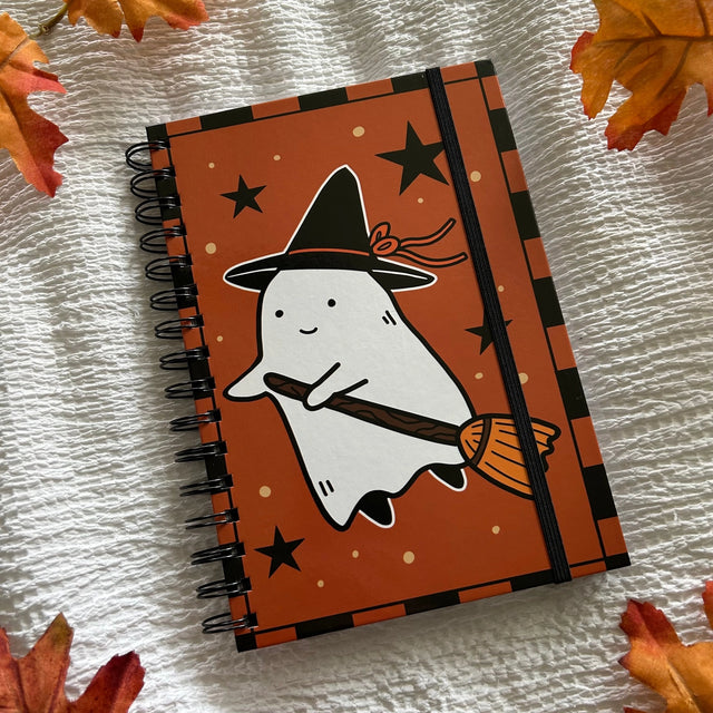 A new A5 notebook featuring a ghost dressing up as a witch!

This hardcover notebook comes lined and with an elastic band. There are 96 double sided pages.