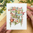 Postcard featuring my original watercolor and ink illustration of the various magical creatures, tiny fairies, and enchanted items nestled on the shelves of a fairy witch, including a magical swan who loves to make potions, a plethora of mushrooms, and a tiny acorn fairy house.