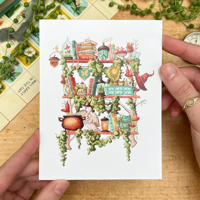 Postcard featuring my original watercolor and ink illustration of the various magical creatures, tiny fairies, and enchanted items nestled on the shelves of a fairy witch, including a magical swan who loves to make potions, a plethora of mushrooms, and a tiny acorn fairy house.