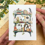 Postcard featuring my original watercolor and ink illustration of the oddities, spooky creatures, and enchanting books tucked away on the shelves of a gothic witch, including a gargoyle enjoying a book, a snake chatting with a spider, and a mysterious ghost.