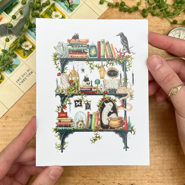 Postcard featuring my original watercolor and ink illustration of the oddities, spooky creatures, and enchanting books tucked away on the shelves of a gothic witch, including a gargoyle enjoying a book, a snake chatting with a spider, and a mysterious ghost.