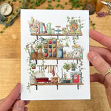 Postcard featuring my original watercolor and ink illustration of the vintage oddities and books tucked away in the shelves of a potter, including glaze test tiles, a tiny kiln, and a bowl of sponges.