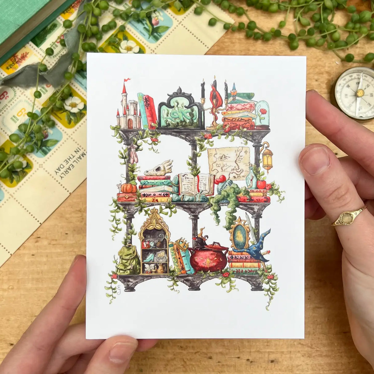Postcard featuring my original watercolor and ink illustration of the various enchanted items collected by a storybook witch as she travels throughout all your favorite fairytales, including a charming castle, a glass-encased rose, and a brightly colored dragon, all nestled on stone shelves that evoke mysterious castle corridors covered in rose vines.
