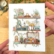 Postcard featuring my original watercolor and ink illustration of the vintage oddities and books tucked away in the shelves of a vintage writer, including a Poe pencil holder, a stained glass lamp, and a blue typewriter.