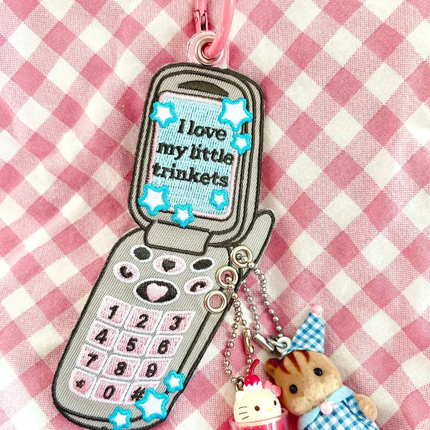 These cute embroidered keychains attach with a colorful ring clasp and are perfect for attaching to your keys or bag to bring with you on all of your adventures!

This particular cell phone design is inspired by Y2K and 2000s. It features extra silver grommets to hang more keychains and showcase your favorite charms! Perfect for any trinket and knick knack hoarder.

Includes one keychain only.
Embroidered on both sides.&nbsp;
Materials: Cotton, Polyester, Brass