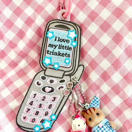 These cute embroidered keychains attach with a colorful ring clasp and are perfect for attaching to your keys or bag to bring with you on all of your adventures!

This particular cell phone design is inspired by Y2K and 2000s. It features extra silver grommets to hang more keychains and showcase your favorite charms! Perfect for any trinket and knick knack hoarder.

Includes one keychain only.
Embroidered on both sides.&nbsp;
Materials: Cotton, Polyester, Brass
