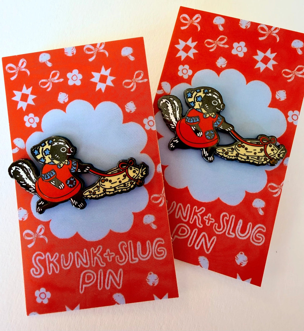 A Skunk and their friend the Slug take a walk through the forest.

This hard enamel pin measures approximately 1.75" and features a rubber clasp for easy closure and two back posts so pin stays where you stick it. Comes with a back card.