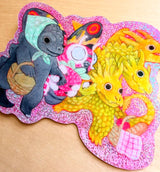 Three Kaiju friends go for a picnic.

This vinyl glittery sticker is weather and waterproof-stick it on a notebook, bike, or car- it's going to stick around! Heck, throw it on a water bottle and through the dishwasher. This sticker can go anywhere. Sticker measures 3.25" x 4.5" Printed in USA.