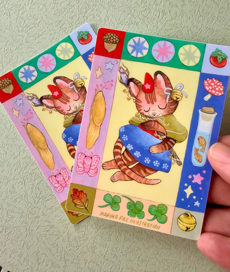 Folk art and magical elements frame a magical cat on this vinyl sticker.

This vinyl matte sticker is weather and waterproof-stick it on a notebook, bike, or car- it's going to stick around! Heck, throw it on a water bottle and through the dishwasher. This sticker can go anywhere. Sticker measures 4.5" x 3.25" Printed in USA.