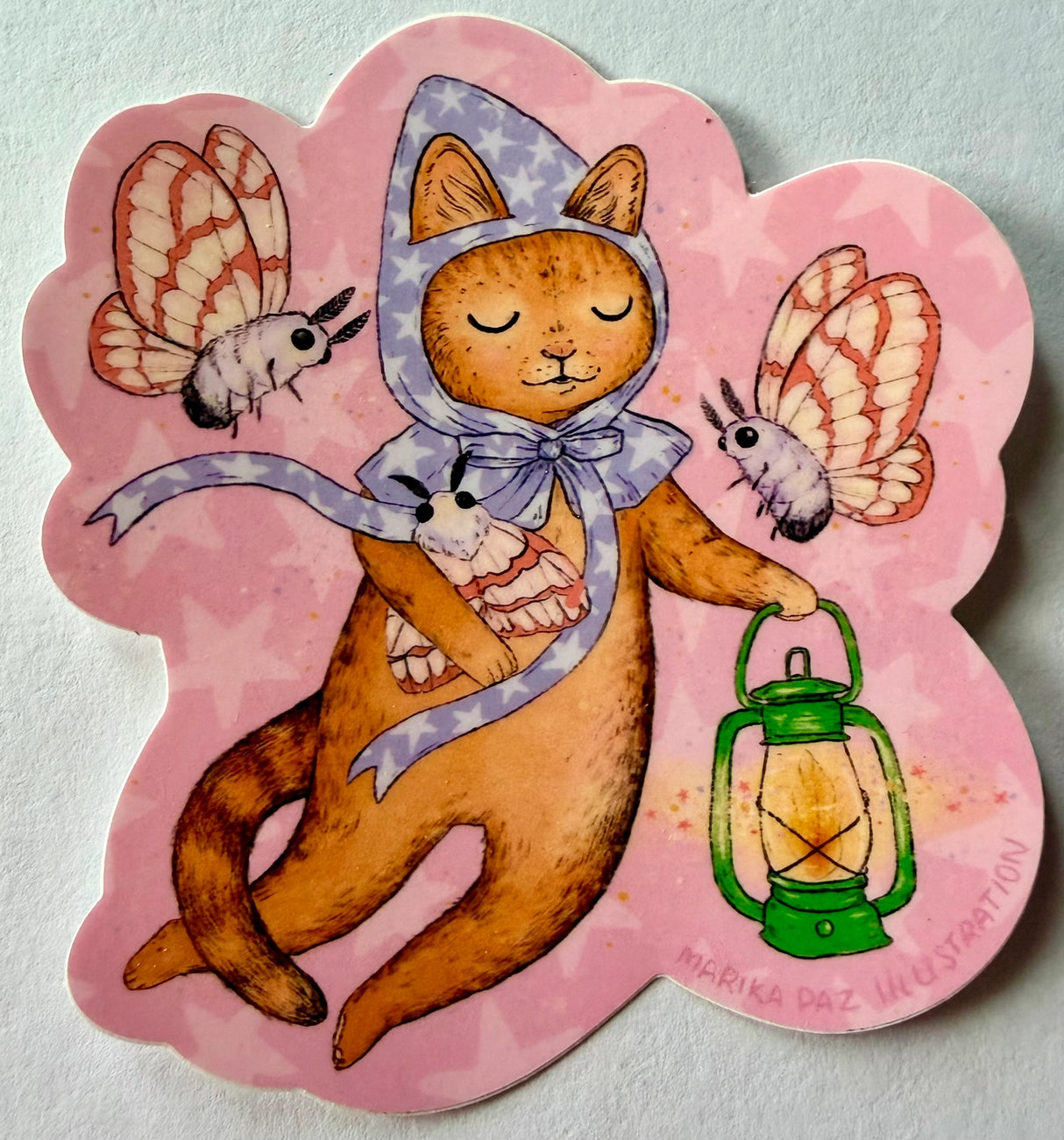A cat and his lantern attract moths as they float amongst the stars.

This vinyl matte sticker is weather and waterproof-stick it on a notebook, bike, or car- it's going to stick around! Heck, throw it on a water bottle and through the dishwasher. This sticker can go anywhere. Sticker measures 3.5" x 4.5" Printed in USA.