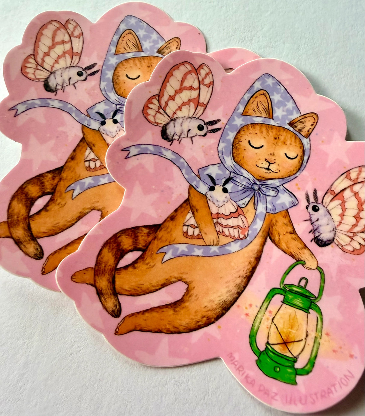 A cat and his lantern attract moths as they float amongst the stars.

This vinyl matte sticker is weather and waterproof-stick it on a notebook, bike, or car- it's going to stick around! Heck, throw it on a water bottle and through the dishwasher. This sticker can go anywhere. Sticker measures 3.5" x 4.5" Printed in USA.