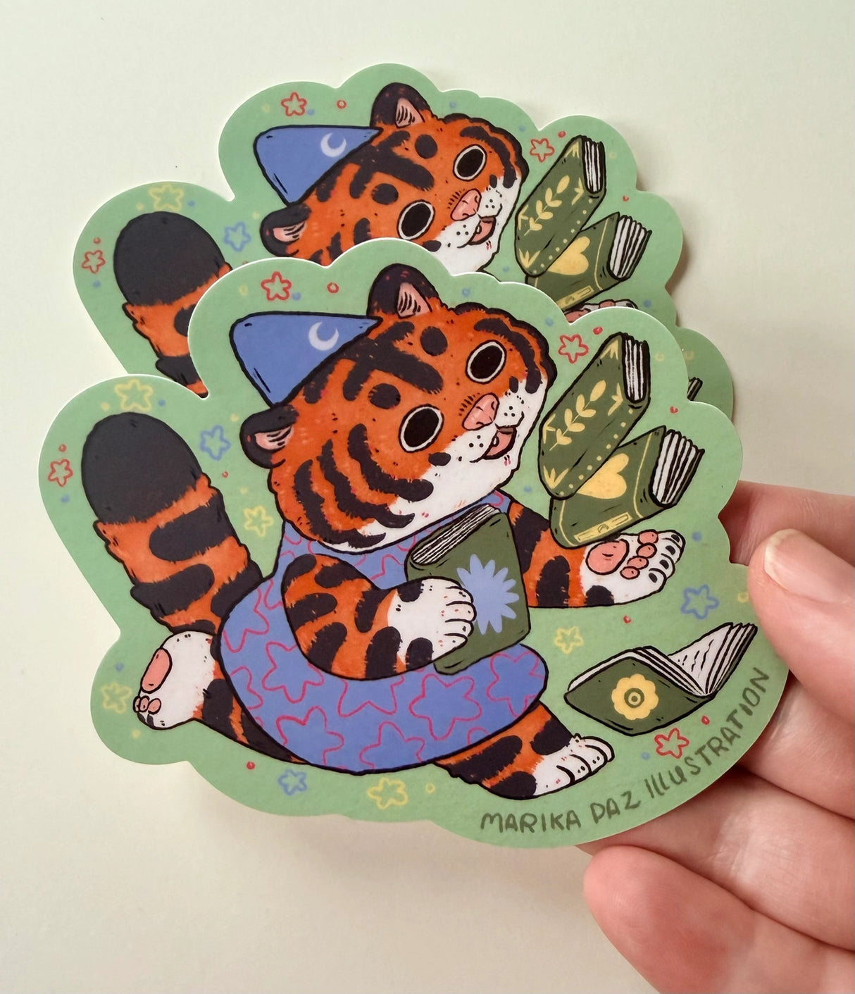 This tiger loves books so much, she can't hold them all at once!

This vinyl matte sticker is weather and waterproof-stick it on a notebook, bike, or car- it's going to stick around! Heck, throw it on a water bottle and through the dishwasher. This sticker can go anywhere. Sticker measures 4" x 4" Printed in USA.