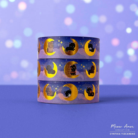 Add a magical glow to your projects with the Moon Cats Gold Foil Washi Tape. Featuring adorable cats surrounded by moon and star designs, this tape shines with elegant gold foil accents. Perfect for adding a cute, celestial touch to planners, gifts, and crafts.

Gold Foil Details&nbsp;
One 10-meter long roll of washi tape
15mm wide
32mm paper core