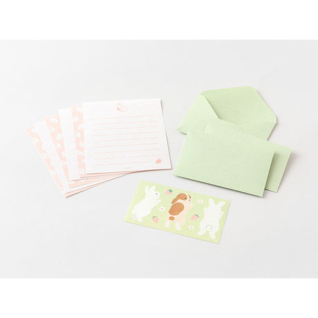 The set shows a rabbit stretching and chasing a strawberry. The stationery paper is a soft pink color inspired by strawberries. The ruled lines are designed to evoke the image of a rabbit bouncing around.