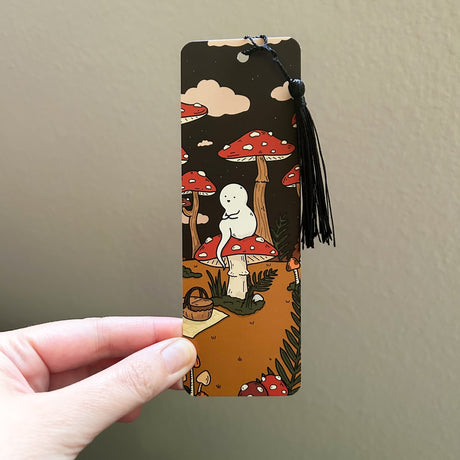 Bookmark featuring a little ghost sitting in a mushroom forest with a picnic basket, awaiting a friend.
