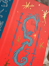 This is a blank 200 page notebook/sketchbook with thin ivory Munken paper perfect for light sketching or writing. Part of a fantasy collection called Woodfolk.

The cover is fluorescent pink/orange and has a smooth matte finish with gold foiling on the front and back. Plus it has a blue fabric spine with white embossing, adding to the charm of the book. Best for pencils, light pens, and generally light mediums, as thick markers or water can bleed. Not recommended for gouache or heavy marker use.