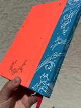 This is a blank 200 page notebook/sketchbook with thin ivory Munken paper perfect for light sketching or writing. Part of a fantasy collection called Woodfolk.

The cover is fluorescent pink/orange and has a smooth matte finish with gold foiling on the front and back. Plus it has a blue fabric spine with white embossing, adding to the charm of the book. Best for pencils, light pens, and generally light mediums, as thick markers or water can bleed. Not recommended for gouache or heavy marker use.