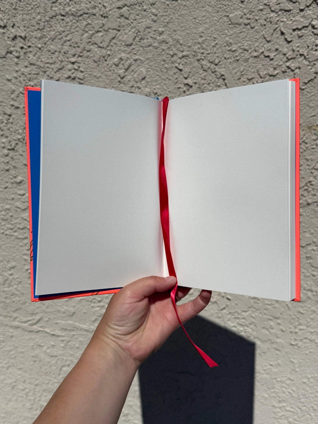 This is a blank 200 page notebook/sketchbook with thin ivory Munken paper perfect for light sketching or writing. Part of a fantasy collection called Woodfolk.

The cover is fluorescent pink/orange and has a smooth matte finish with gold foiling on the front and back. Plus it has a blue fabric spine with white embossing, adding to the charm of the book. Best for pencils, light pens, and generally light mediums, as thick markers or water can bleed. Not recommended for gouache or heavy marker use.