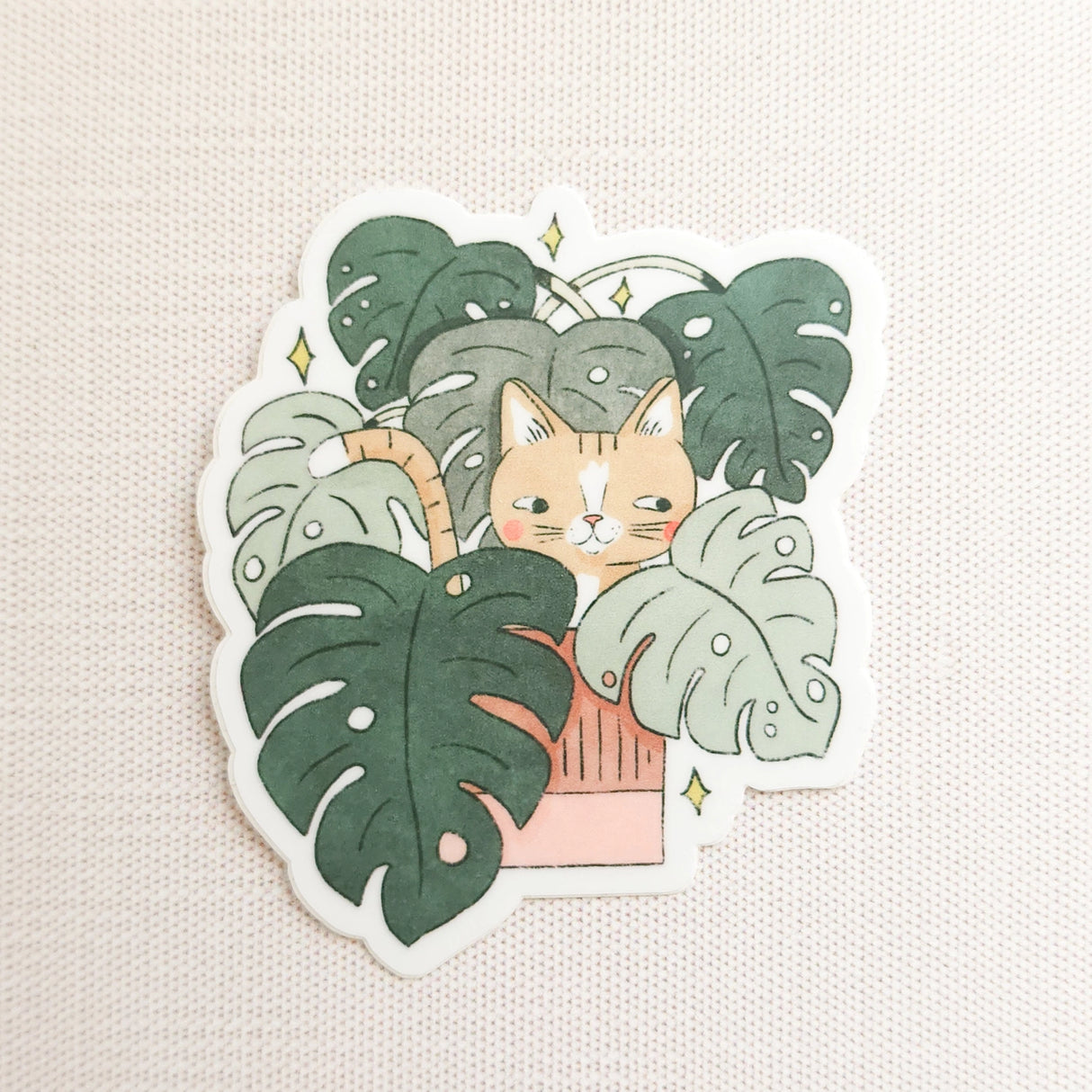 A curious cat settles among lush monstera leaves, tucked into the calm greenery of a Wildflower Woods cottage. This vinyl sticker captures that cozy, plant-filled moment, bringing a touch of quiet charm to your everyday essentials.

Made from durable, waterproof vinyl, this sticker is designed to hold up wherever you place it—whether that’s a water bottle, laptop, or journal you reach for daily.