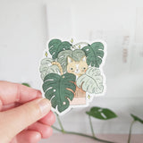 A curious cat settles among lush monstera leaves, tucked into the calm greenery of a Wildflower Woods cottage. This vinyl sticker captures that cozy, plant-filled moment, bringing a touch of quiet charm to your everyday essentials.

Made from durable, waterproof vinyl, this sticker is designed to hold up wherever you place it—whether that’s a water bottle, laptop, or journal you reach for daily.