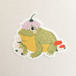A happy little toad pauses among blooming flowers and mushrooms, a small flower worn proudly atop his head. This vinyl sticker captures that lighthearted moment, celebrating comfort, confidence, and being yourself in the everyday.

Made from durable, waterproof vinyl, this sticker is designed to hold up wherever you place it—whether that’s a water bottle, laptop, or journal you reach for daily.