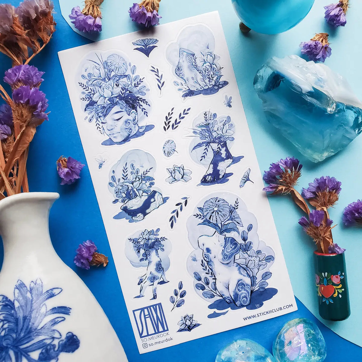 💐🌀 Step into @so.meurdok’s surreal garden, where faces, hands, feet, and figures blossom into living bouquets. Lush florals and striking blue details blur the line between body and bouquet, while foil accents trace every elegant curve like enchanted brushstrokes. A tiny art gallery, now in sticker form. Art by: @so.meurdok

Top Coating: Blue foil
Adhesive Layer: Paper
Backing Layer: Paper
6.69" x 3.54".
Weight - 0.03lbs
1 sheet included
