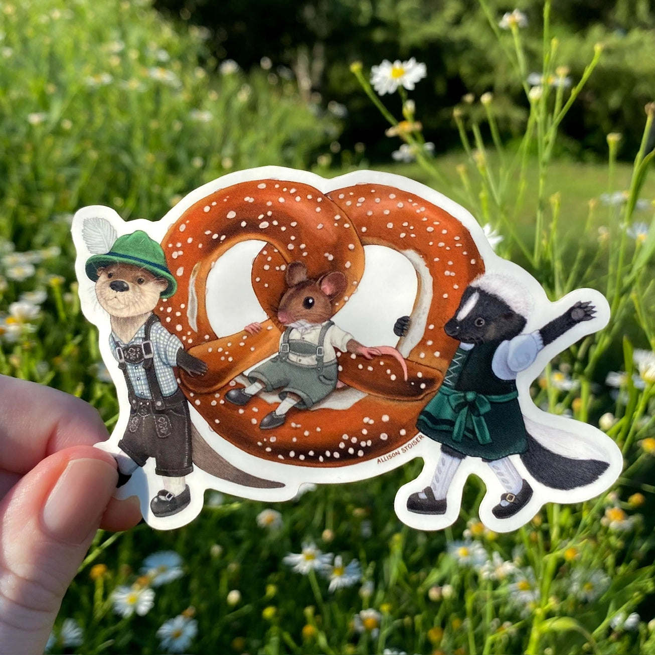 These critters are ready for Oktoberfest! Dressed in their finest lederhosen and dirndl, this otter and skunk are proudly carrying a larger-than-life pretzel. Their mouse pal is just along for the ride!

This die-cut gloss vinyl sticker is durable, weatherproof, and perfect for water bottles, notebooks, laptops, bikes, and all sorts of other surfaces! Make sure to clean and dry the surface thoroughly before applying.