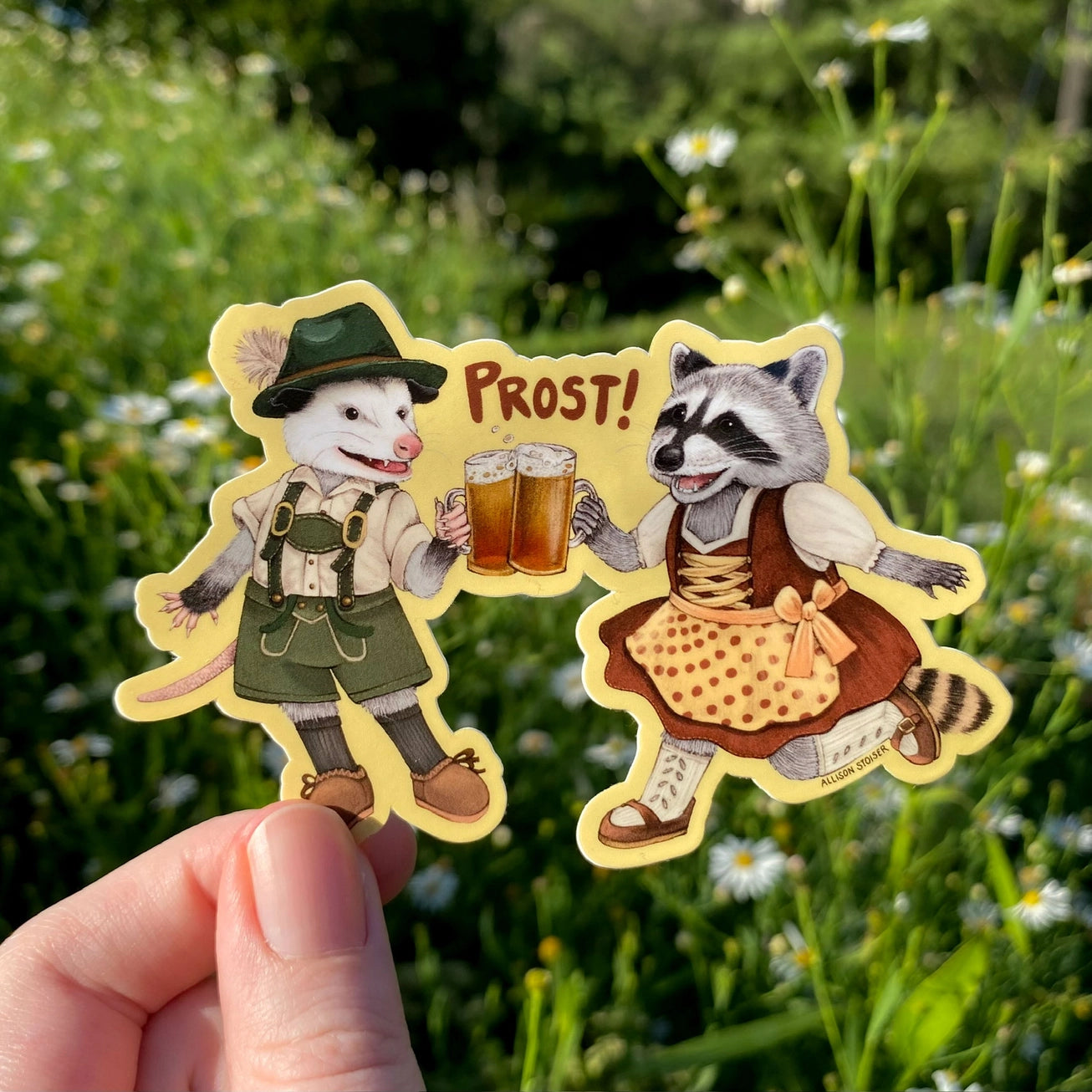 These critters are excited for Oktoberfest! Dressed in their finest lederhosen and dirndl, this opossum and raccoon are having a toast and shouting "Prost!"

This die-cut gloss vinyl sticker is durable, weatherproof, and perfect for water bottles, notebooks, laptops, bikes, and all sorts of other surfaces! Make sure to clean and dry the surface thoroughly before applying.

This sticker is perfect for folks who love opossums, raccoons, cute critters, wildlife, and Oktoberfest