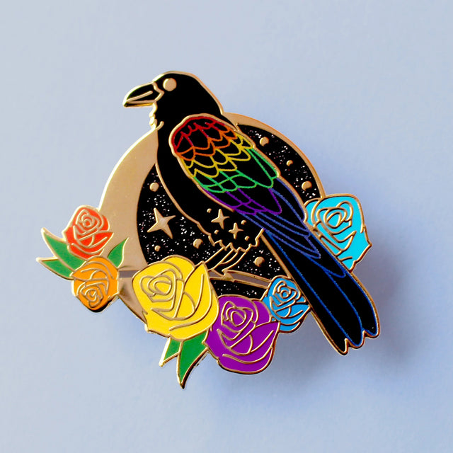 This enamel pin features a black raven with rainbow-coloured wings. It’s sitting on a branch surrounded by rainbow-coloured roses, in front of a glittery moon. The pin is presented on a Glitter Punk backing card and is secured with 2 pin backs.

This pin is part of the Corvid Collection, an 8-part series of bird pins. 

Measurements: 42mm